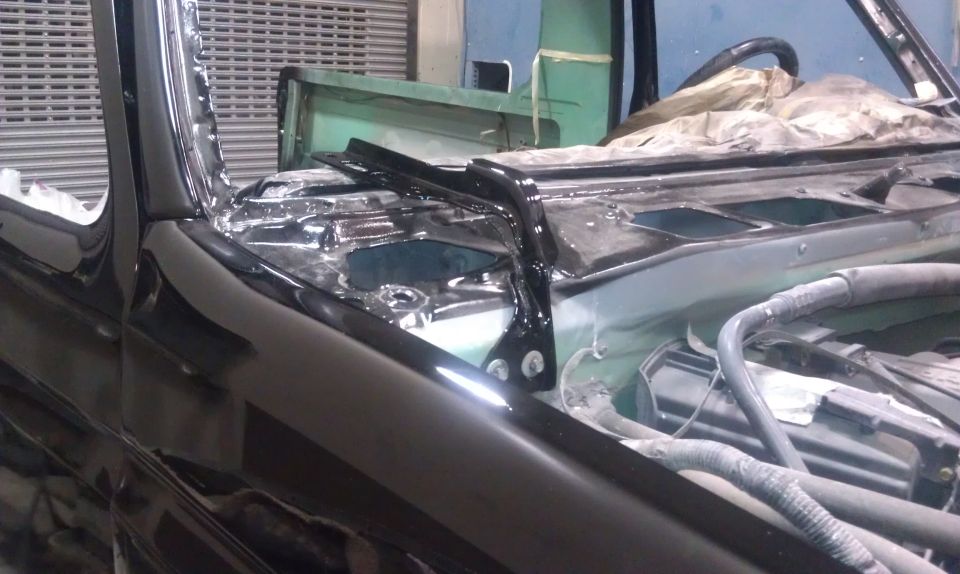 Car hood and windshield area, looks like it's being worked on. Some parts are shiny black, others are green