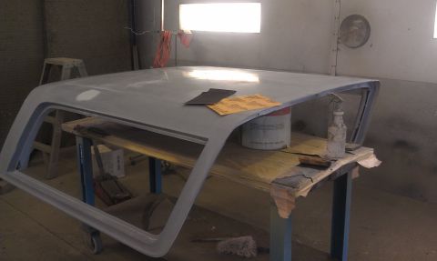 1995 Ford Bronco - A car roof panel is being prepped for paint on a workbench, with sandpaper and a spray bottle nearby.