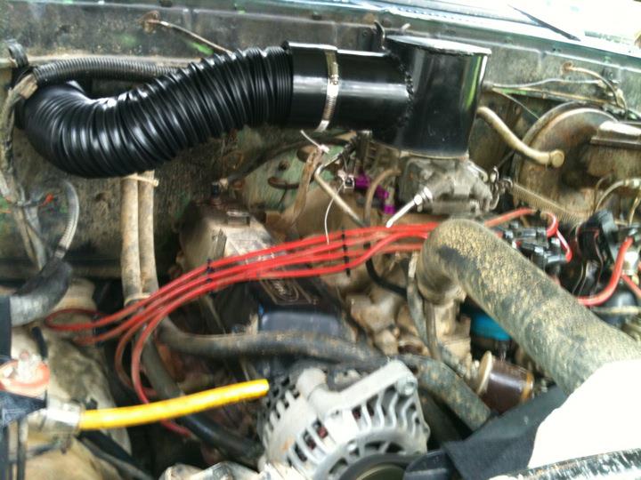Dirty truck engine bay with black air intake tube and red spark plug wires
