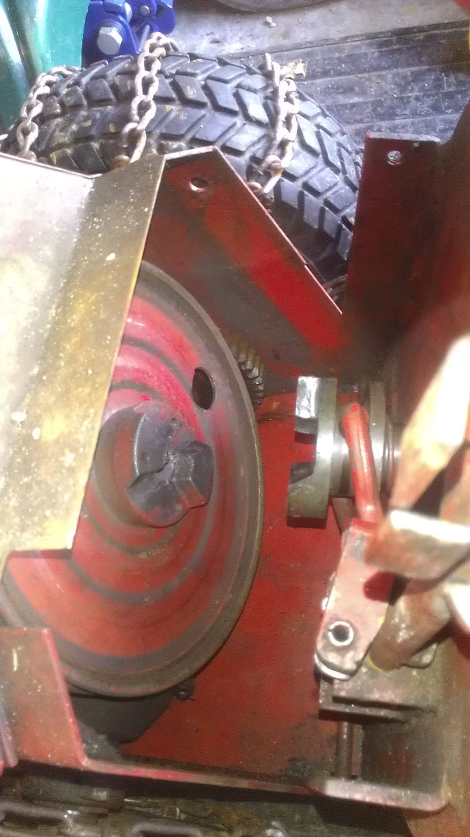 Close-up of a snow blower's red auger pulley and drive mechanism, with a tire and chains visible above