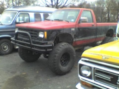 1987 Mazda RX-7 - A modified pickup truck with large off-road tires is parked outdoors.