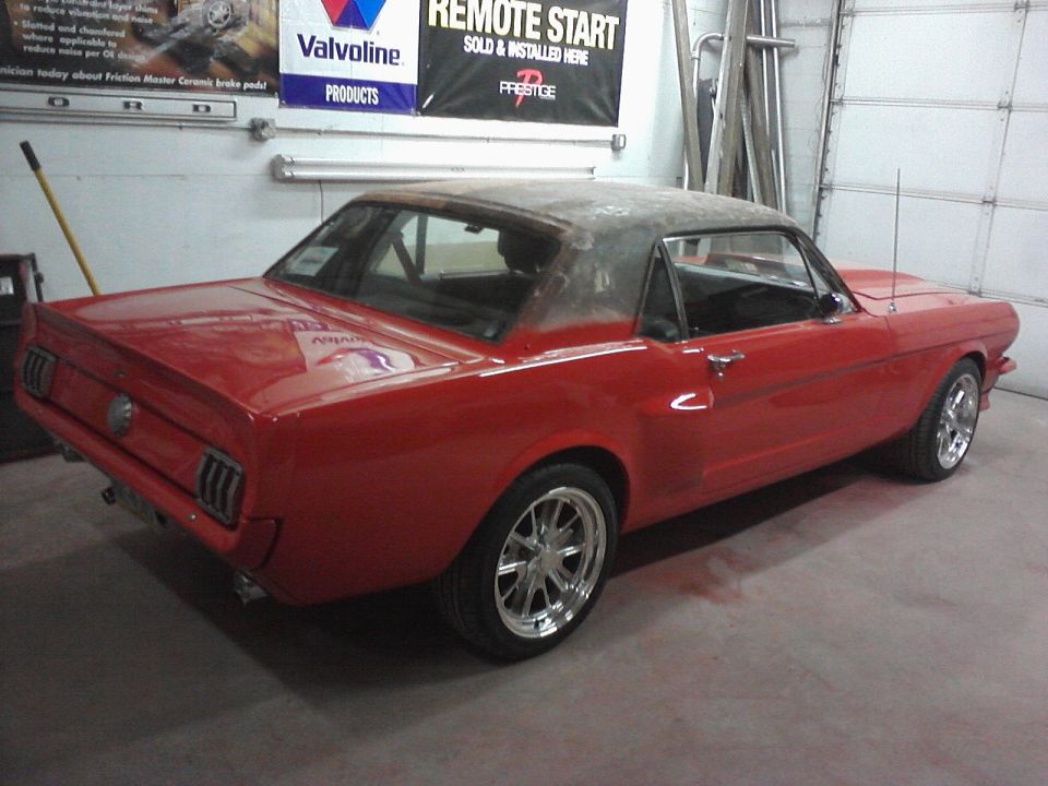 Red 1966 Ford Mustang coupe with a black roof, undergoing restoration, viewed from the rear three-quarter ang…