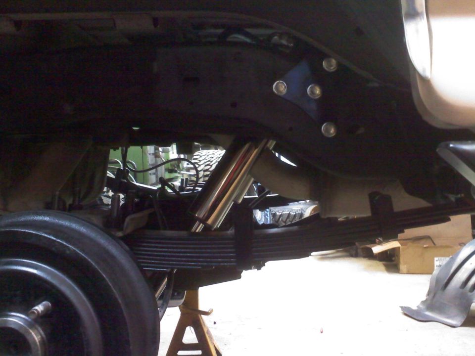 Undercarriage view showing leaf springs, a shock absorber, and part of a wheel. A blue bracket is bolted to the frame