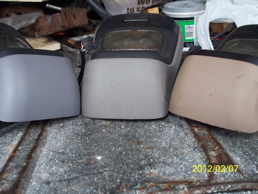 three vehicle interior console pieces, one in tan, two in gray, on a rough surface