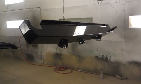 1995 Ford Bronco - A black bumper is suspended in a spray booth, likely undergoing a refinishing process.