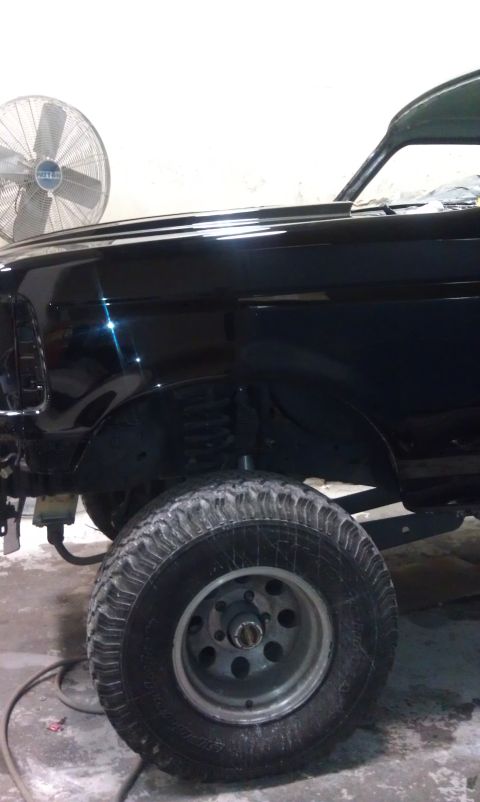 1995 Ford Bronco - Close-up of the front wheel well and fender of a black SUV, showing suspension components.
