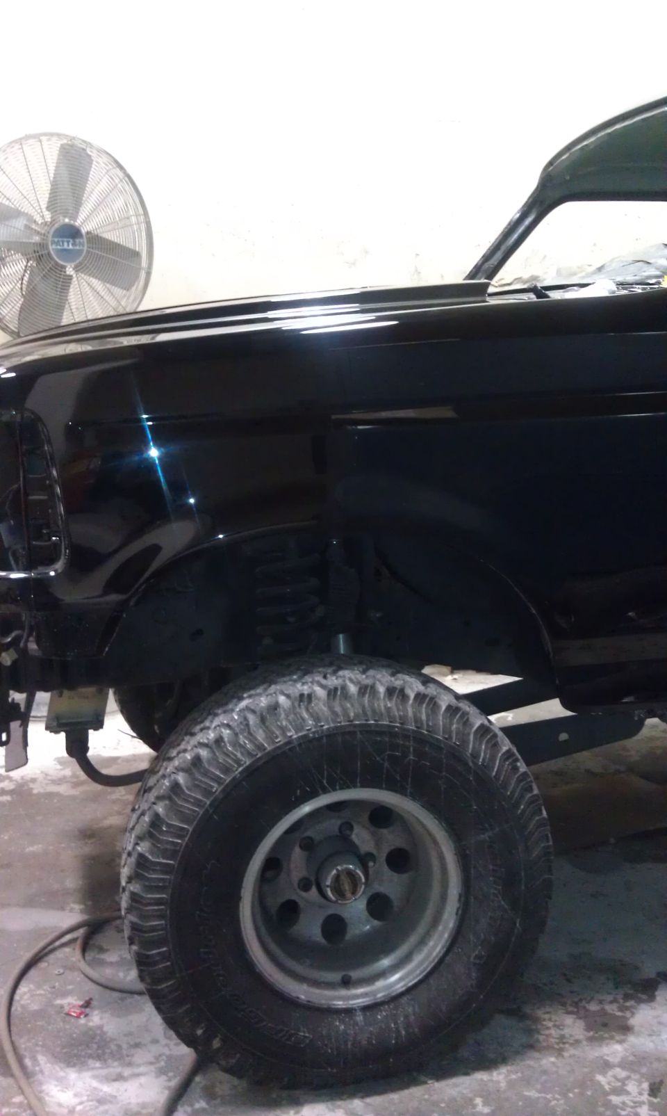 Black SUV, front fender and tire visible. Fan in background