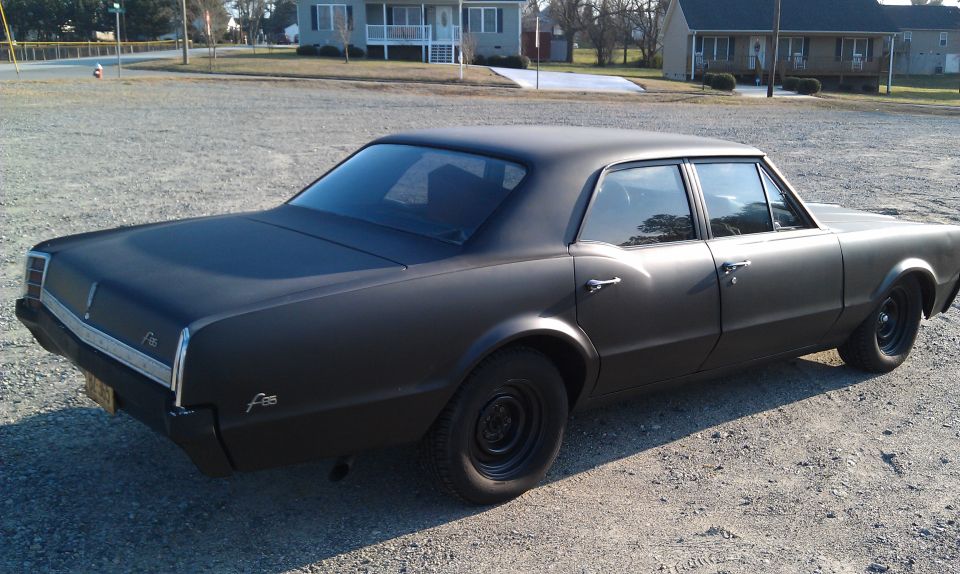 Black sedan parked on gravel lot, rear quarter view