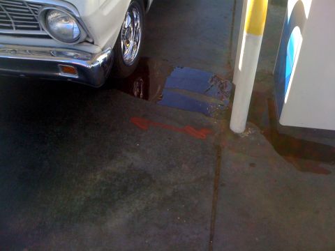 1964 Ford Ranchero - A white car with a chrome grille and bumper is parked on wet concrete, with a red arrow painted on the ground.