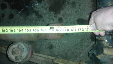 1987 Ford Ranger - A measuring tape is used to measure a rusty suspension part, possibly for replacement or identification.