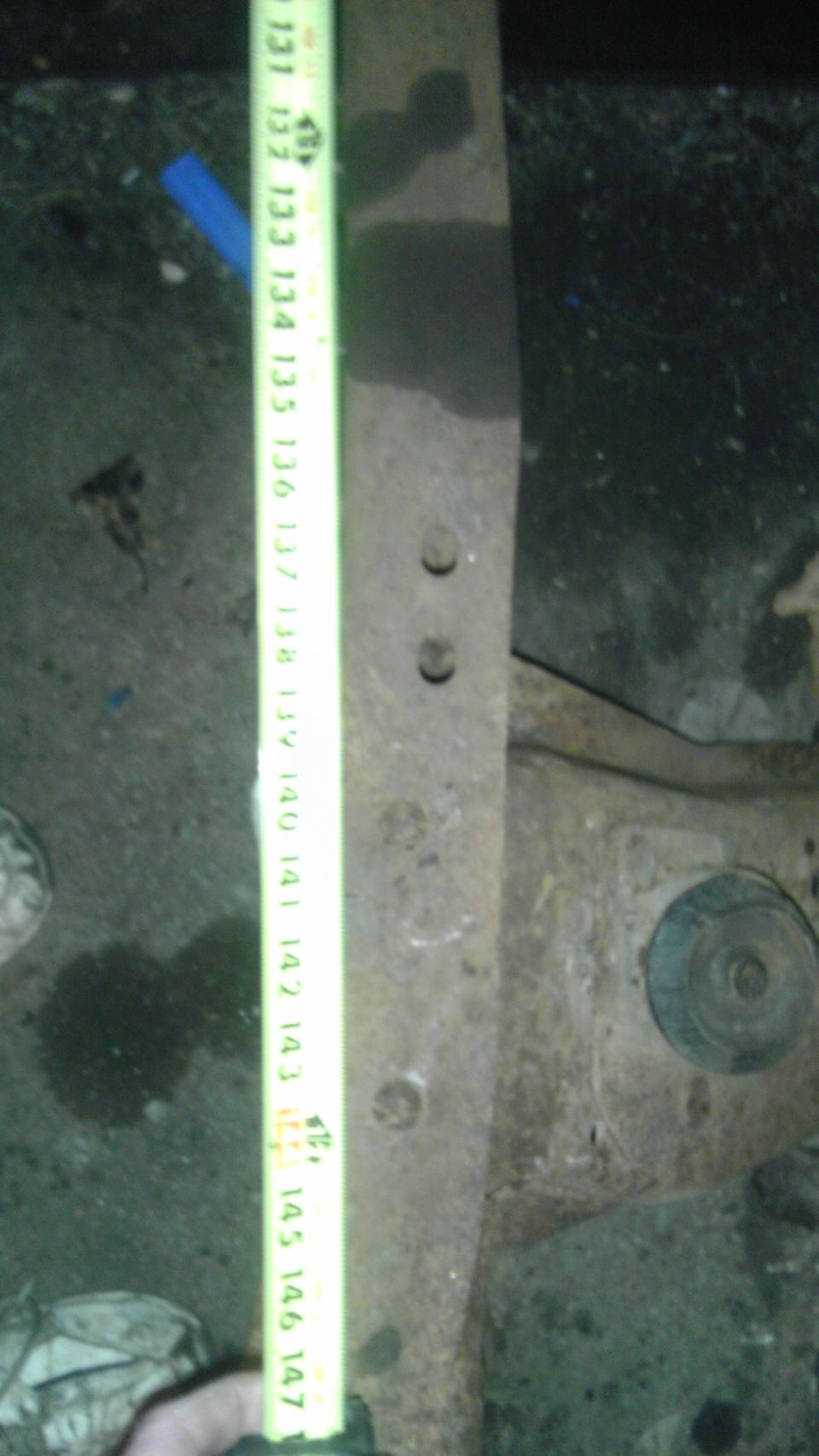 rusted metal suspension component with a yellow measuring tape showing inches from 131 to 147