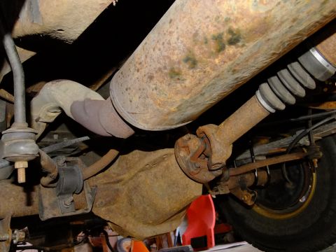 1995 Ford Bronco - Undercarriage view of a heavily rusted rear differential and exhaust system with visible driveshaft.