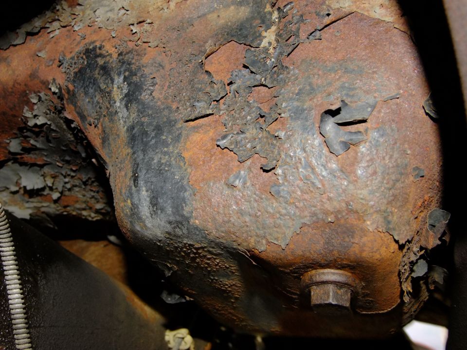 Heavily rusted metal part with peeling paint and a hex bolt