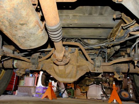 1995 Ford Bronco - Underside view of a heavily rusted 1995 Ford Bronco rear axle assembly supported by orange jack stands.