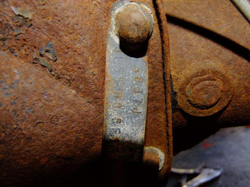 Close-up of a rusty metal tag with stamped numbers on a heavily rusted vehicle chassis component
