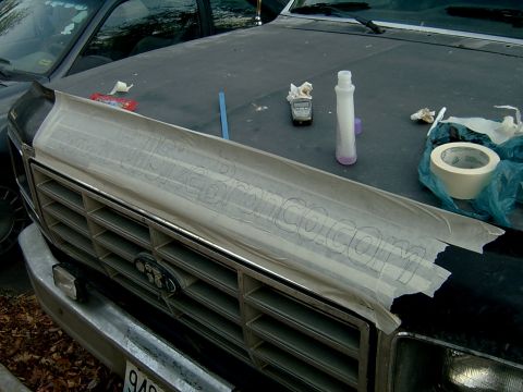 1982 Ford Bronco - Hood protector with a tape stencil for 'Bronco.com' is laid over the grille of a Ford truck.