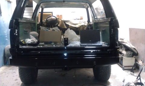 1995 Ford Bronco - The rear of a black Ford Bronco is shown with its tailgate open, revealing a cluttered interior.