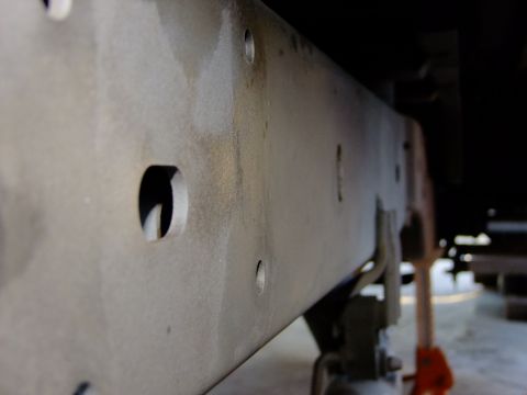 1995 Ford Bronco - Close-up of a vehicle's frame rail, showing mounting holes and surface texture.