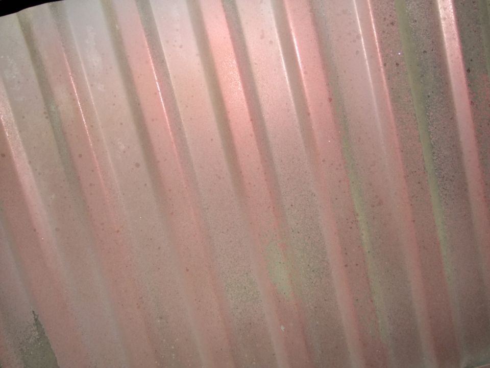Corrugated metal surface with pink and green overspray