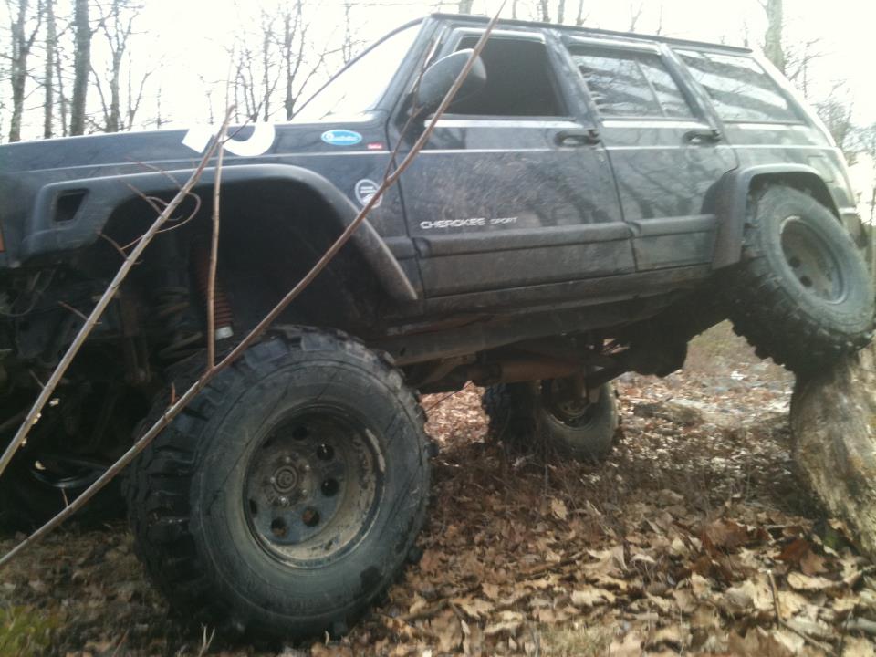 Black Jeep Cherokee Sport climbing over a rock on a wooded trail