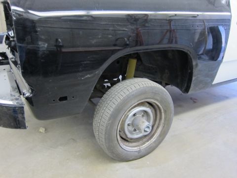 1987 Dodge 1500 - A portion of a black truck's body and wheel is shown, possibly undergoing repairs or restoration.