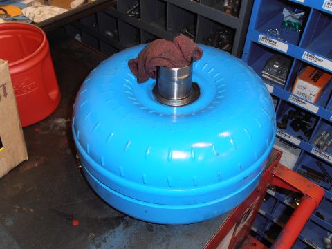 1990 Ford Bronco - A blue torque converter is shown resting on a workbench, with storage bins filled with parts behind it.