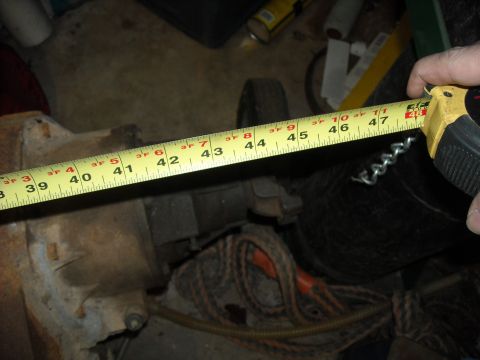 1979 Ford F-150 - A yellow measuring tape is used to measure an unidentified, rusty automotive component in a cluttered garage setting.
