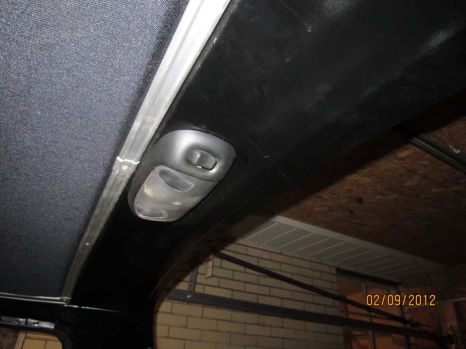 Interior overhead light console with a dark fabric headliner and a metal trim piece
