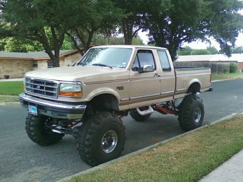 1989 Ford Bronco - This lifted pickup truck, likely a 1992 model based on its grille, is parked on a residential street.