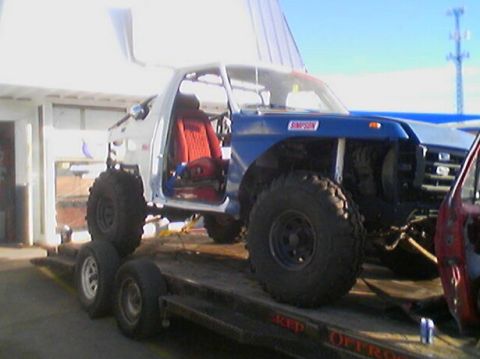 1989 Ford Bronco - A heavily modified truck with a blue hood and red seats is transported on a trailer.