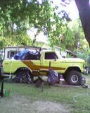 1989 Ford Bronco - A yellow pickup truck with a brown stripe is parked outdoors, appearing to be modified with a lifted suspension.