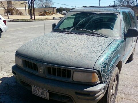 1989 Ford Bronco - A dusty green SUV is parked on a street, showing its front grille and windshield.
