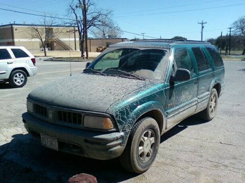 1989 Ford Bronco - This dusty green SUV is parked outside on a sunny day, with another white SUV visible in the background.