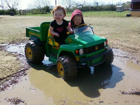 1989 Ford Bronco - Two children ride in a green toy John Deere Gator through muddy terrain.