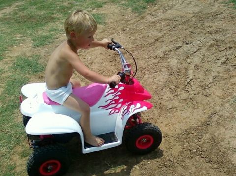 1989 Ford Bronco - A young boy rides a small, four-wheeled toy vehicle outdoors on a dirt path.