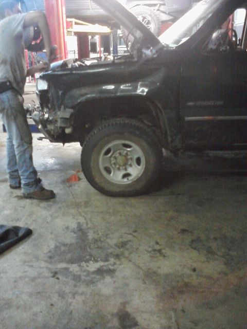 1989 Ford Bronco - A mechanic is repairing the front fender of a black Chevrolet 2500 HD truck in a garage.