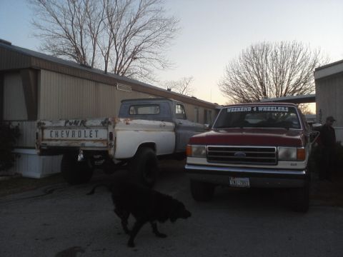 1989 Ford Bronco - Two pickup trucks are parked outside a mobile home, with a dog in front of them.