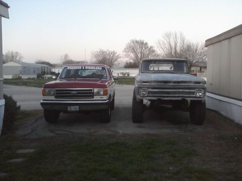 1989 Ford Bronco - Two trucks, a red Ford Bronco and a gray older model, are parked next to each other.