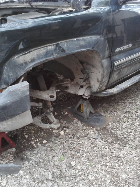 1989 Ford Bronco - A dark green truck's front suspension is exposed while it is supported by jack stands.