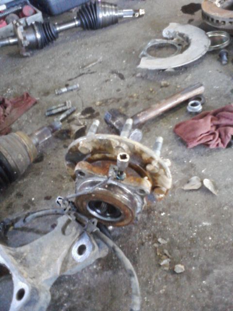 1989 Ford Bronco - Vehicle hub and axle components are laid out on the floor, likely during a repair or maintenance process.