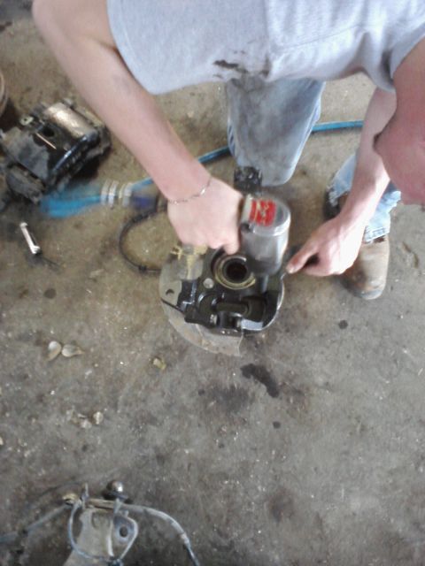 1989 Ford Bronco - A person is using an impact wrench on a vehicle's brake caliper assembly in a garage setting.