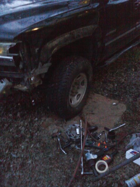 1989 Ford Bronco - A dark SUV with significant front-end damage sits on the ground with tools nearby, suggesting repairs are underway.