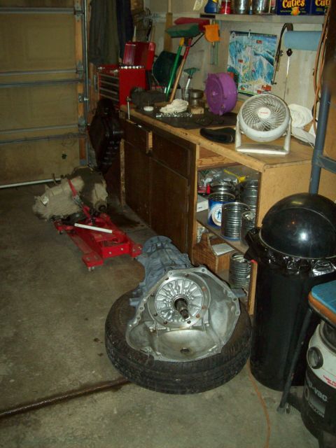 1993 Ford F-150 - Garage scene with a transmission on a tire and another on a jack, next to a workbench with various tools and a fan.