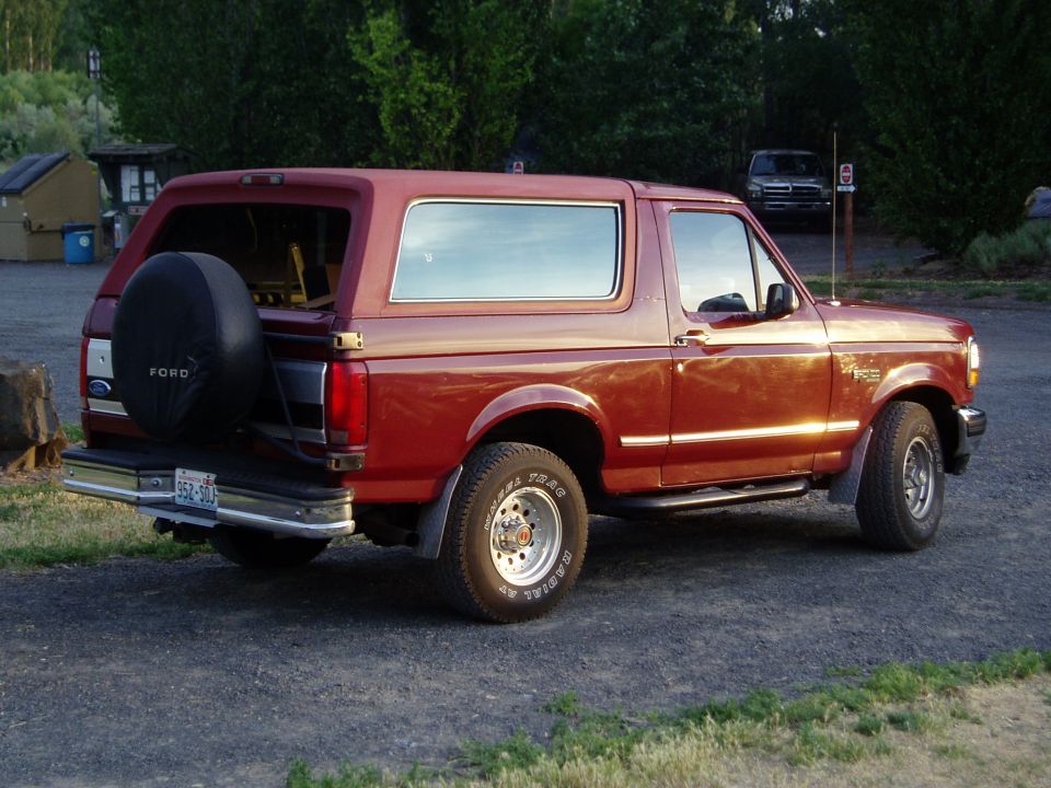 1993 Ford Bronco parked outside, spare tire on rear door. Another vehicle is visible in the background