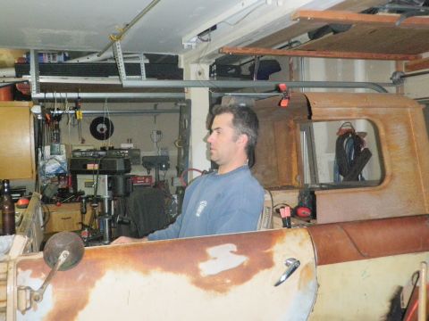 1961 International Scout 800 - Man sits in the cab of a rusty truck, possibly undergoing restoration. Tools and equipment are visible in the background.