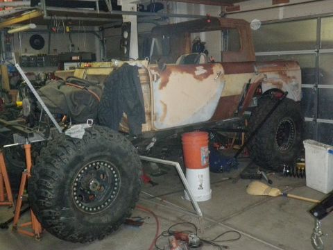 1961 International Scout 800 - Side view of a vintage pickup truck body with significant rust and large tires, in a workshop setting.