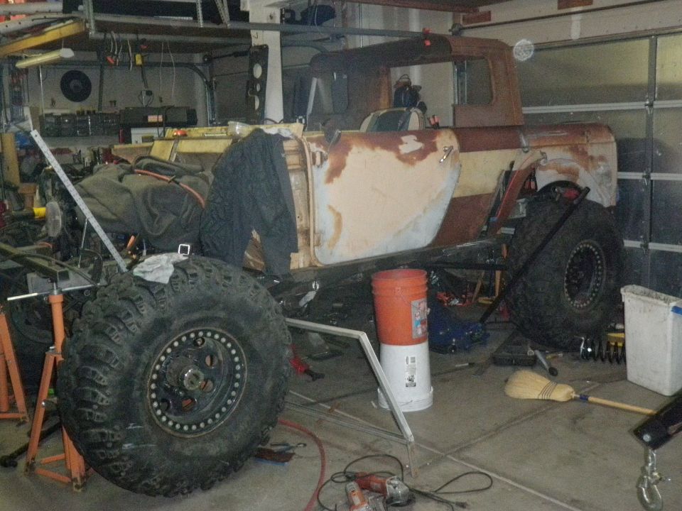 Rusty pickup truck body with large off-road tires, undergoing restoration in a garage