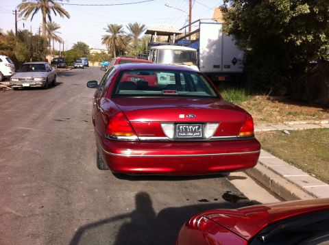 1998 Ford Crown Victoria - A red sedan is parked on a street with other vehicles and palm trees visible.