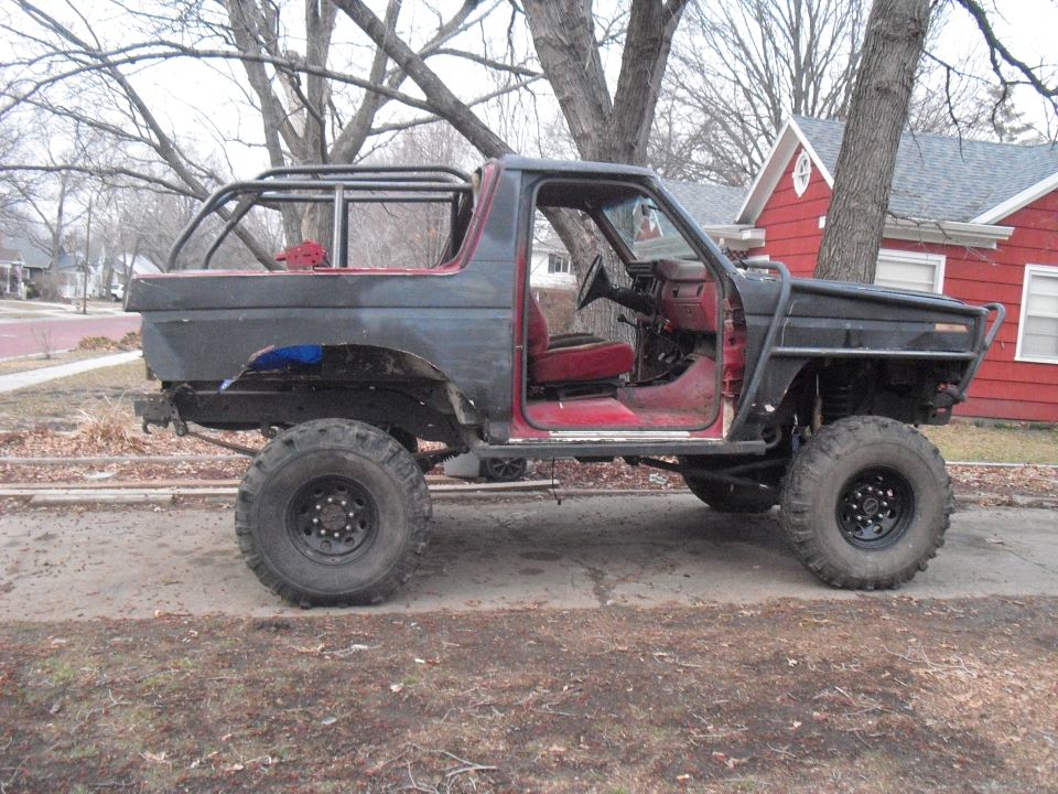 Modified Ford Bronco with roll cage, custom bumpers, and large tires, side view