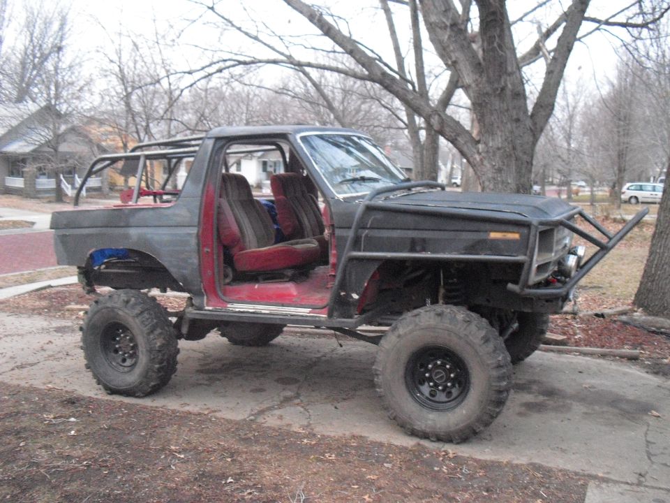 Modified SUV with roll cage, large tires, and custom bumper. Doors are removed, showing red interior seats